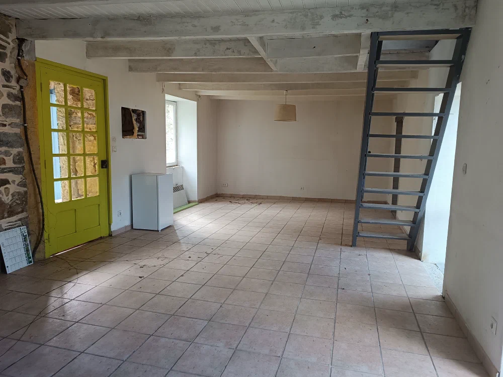 Le séjour carrelé avec sa porte vitrée vert anis et l'échelle de meunier métallique qui mène à l'étage