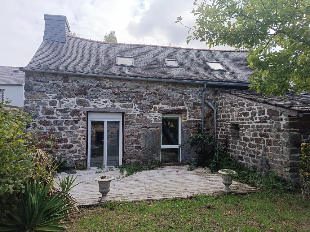 La façade arrière de la maison, avec sa terrasse en bois, ses portes vitrées et la dépendance en pierre attenante